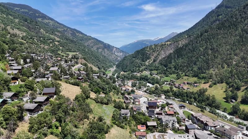 Cluster of houses in a mountainous region, green meadows, and steep hills.