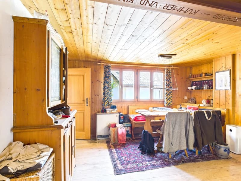 Cozy wooden cabin interior with a fireplace, wooden walls and ceiling, large windows, dining table, and various household items and furniture