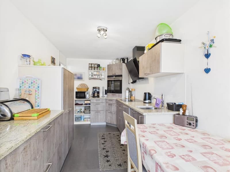 Modern kitchen with gray cabinets, white countertops, built-in appliances including a dishwasher, and various kitchen accessories and decor items.