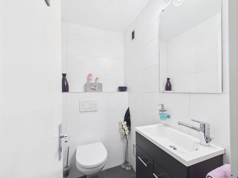 White tiled walls, black vanity unit with sink, toilet, shelves with decorative items