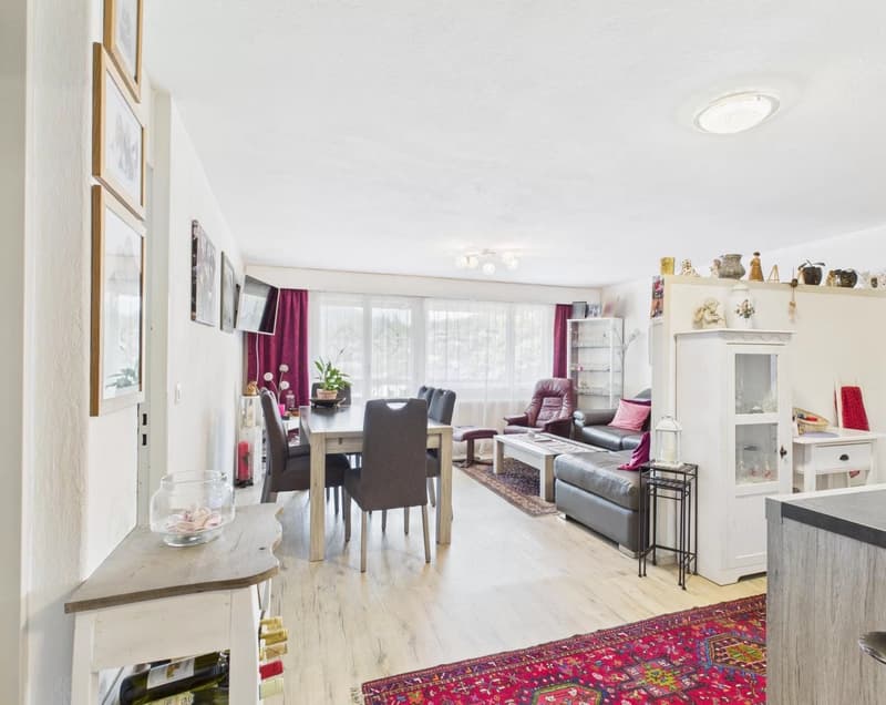 Open-concept living room and dining area, hardwood floors, large windows, purple curtains, leather sofa, dining table with chairs, shelving unit with decor, rug