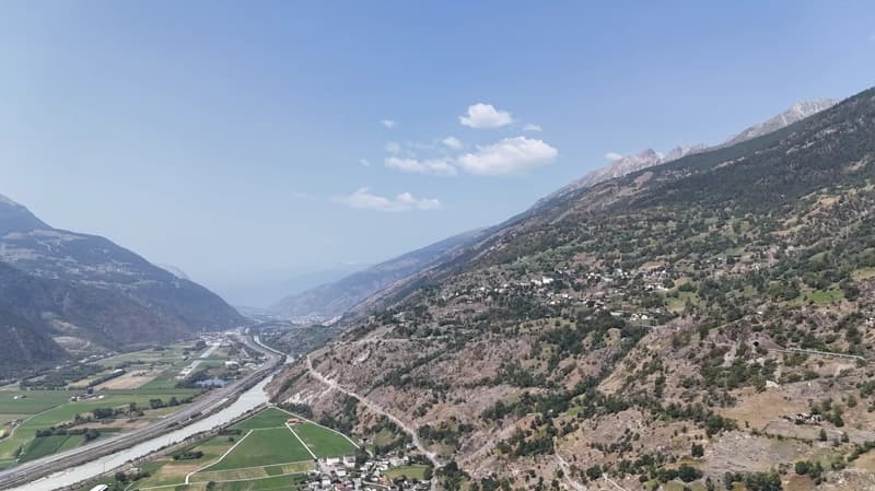 Mountain valley with river, surrounded by mountains, green fields, small settlement, clear sky, scattered clouds