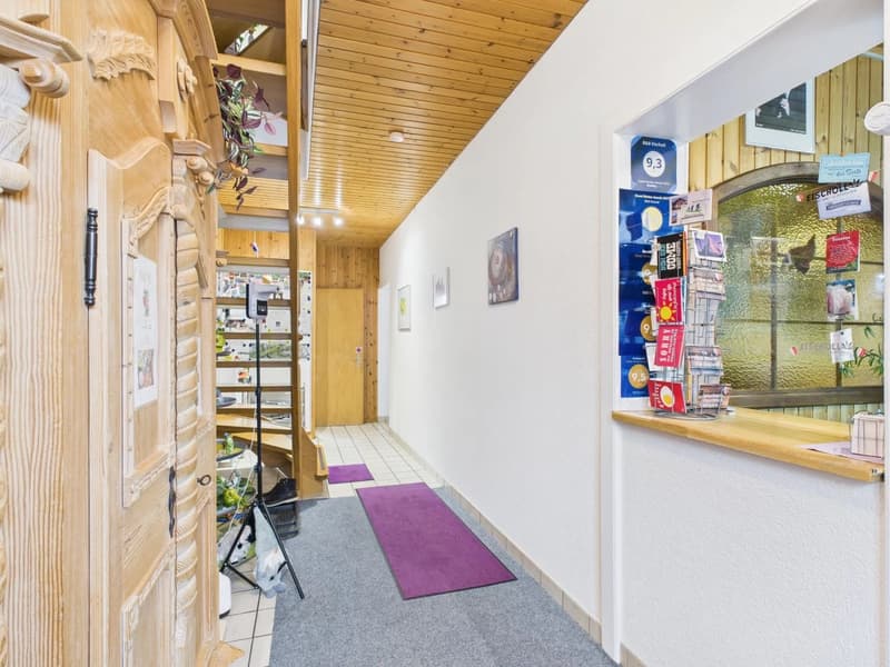 long corridor with wooden door, violet rugs, white tiles, wooden ceiling, picture frames on the wall, white and purple boxes on a shelf