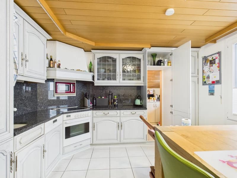 a kitchen with white cabinets, granite countertops, a microwave, a stove, and an oven, a wooden table, and a green chair