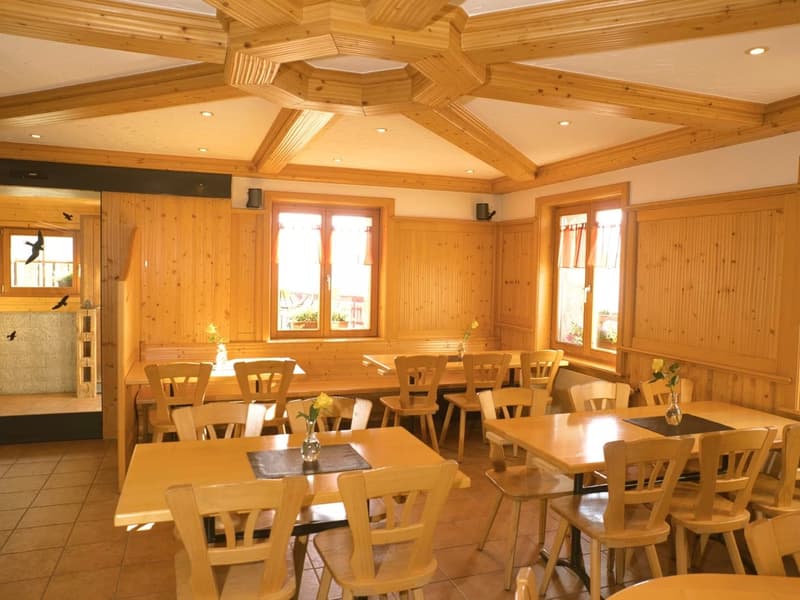 wooden room with tables and chairs, wooden ceiling, yellow flowers in vases, wooden walls, windows with curtains