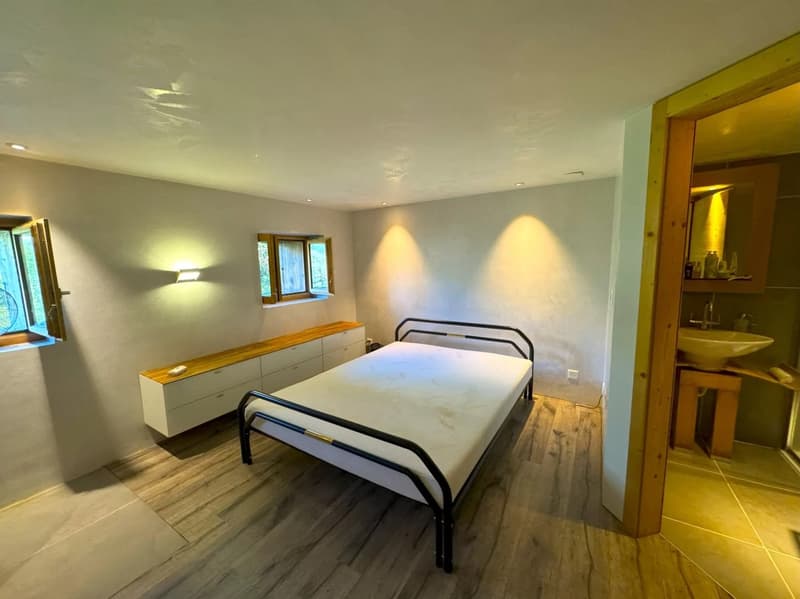 wooden floor, bed with metal frame, wall mounted lamp, white wardrobe, two small windows