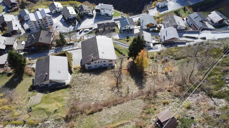 Aerial view of a village with multiple buildings, some with parking spaces, and some with garages