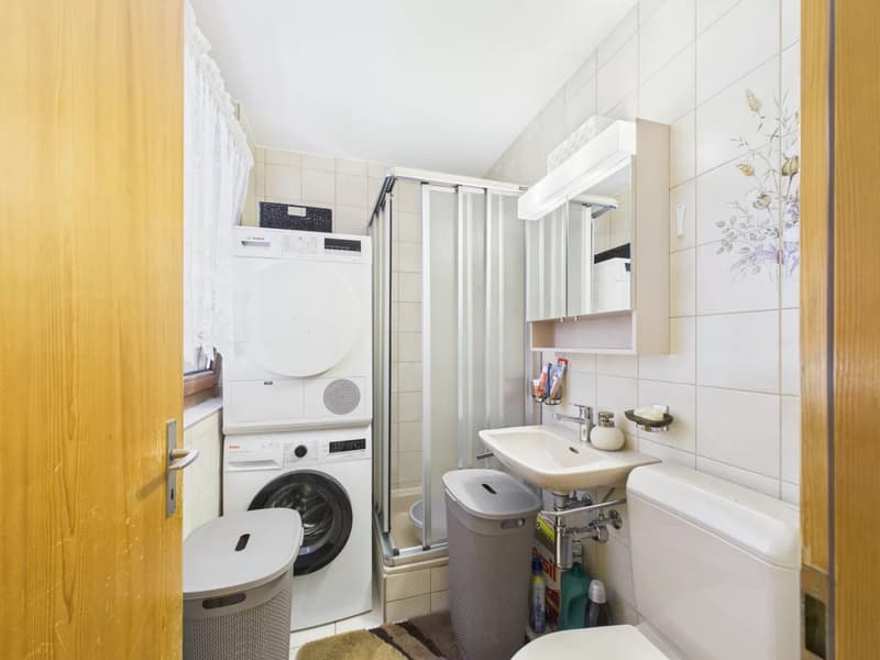 tiled walls, white sink, washing machine, shower, trash bins, toilet