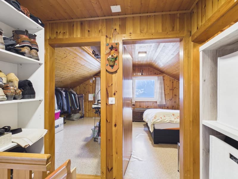 Wooden attic room with bed, small closet, wooden shelves, and a window