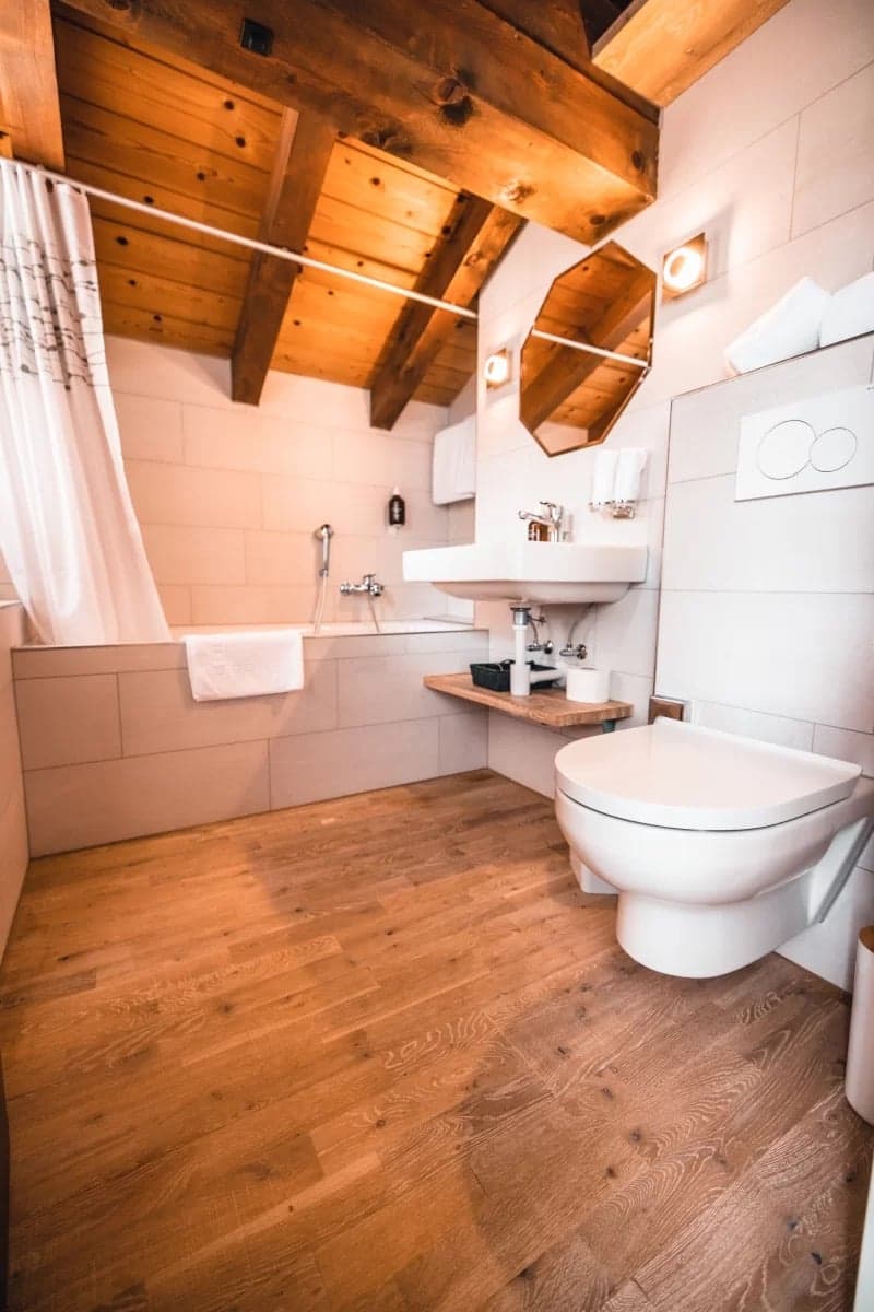 Bathroom with wooden floor, white walls, bathtub, toilet, sink, mirror, wooden ceiling