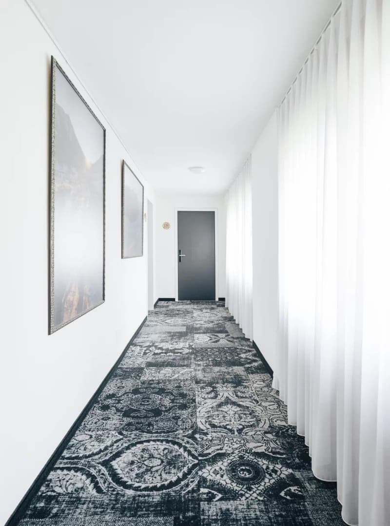 white walls, gray door, patterned carpet, white curtains, two large framed pictures