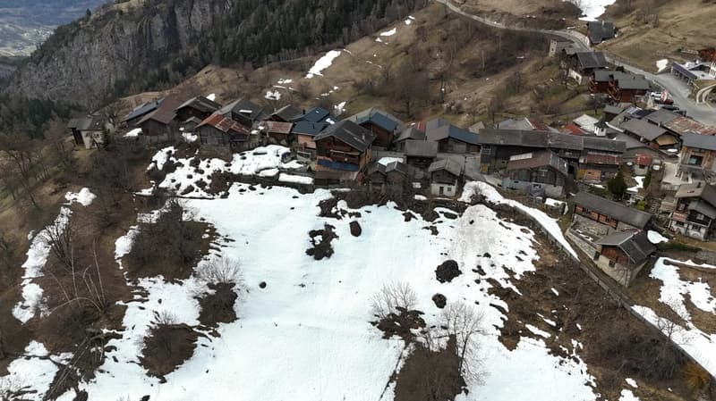 Cluster of wooden houses on a snowy mountain slope, surrounded by trees and snow