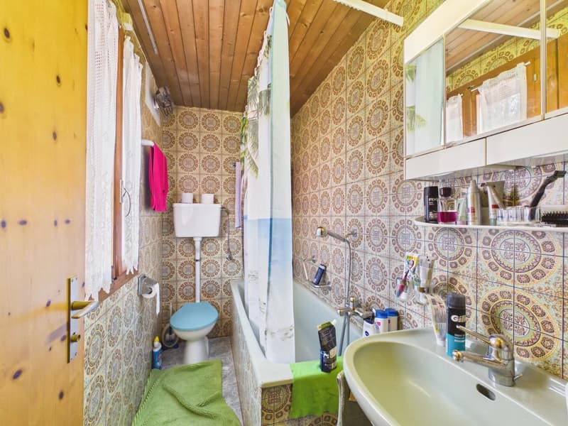 Bathroom with wooden ceiling, tiled walls, bathtub, toilet, sink, shower curtain, towels, toiletries