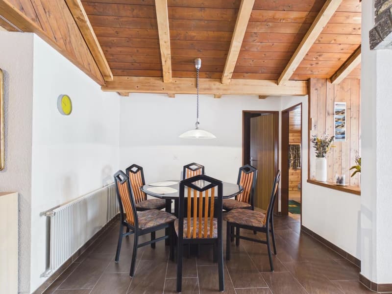 Dining room with wooden ceiling, round table, 6 chairs, radiator, hanging lamp, clock, window with plants
