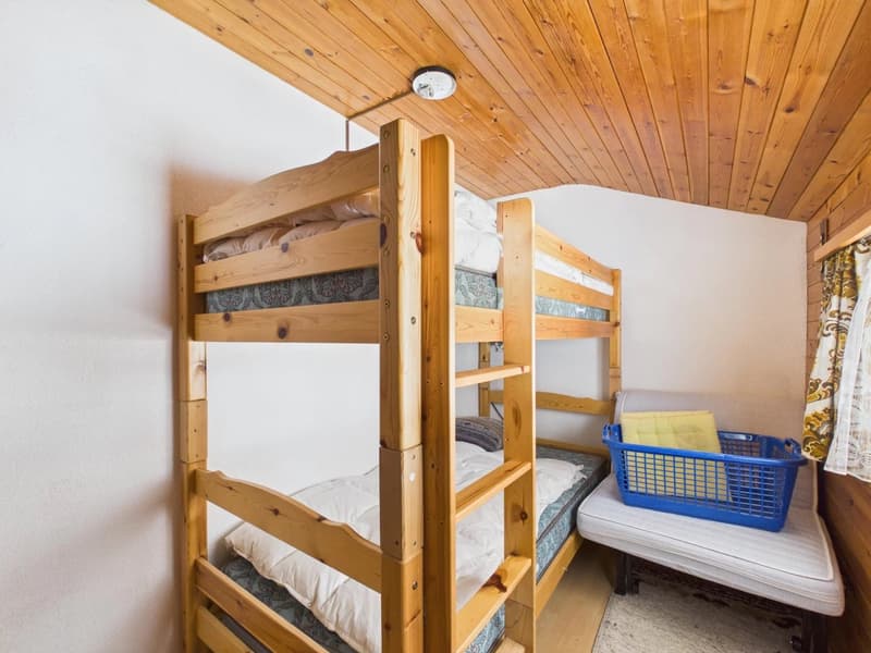 Two wooden bunk beds, white walls, wooden ceiling, white mattress, blue basket, white curtains