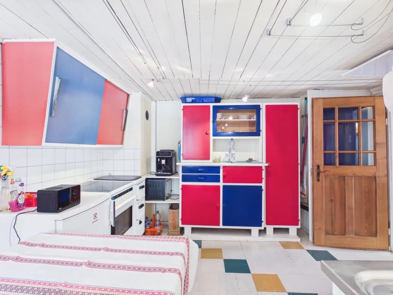 kitchen with white appliances, red and blue cabinets, white tiled walls, wooden door, small bed
