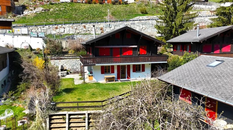 Swiss-style house, red shutters, wooden balcony, stone wall, green lawn, wooden bench, small garden