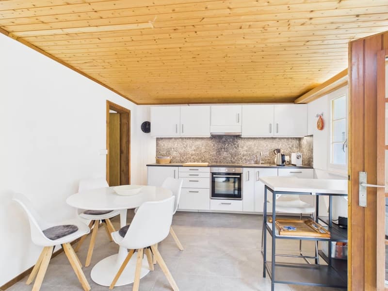 modern kitchen with white cabinets, wooden ceiling, white dining table, white chairs, oven, sink, countertop, basket, clock