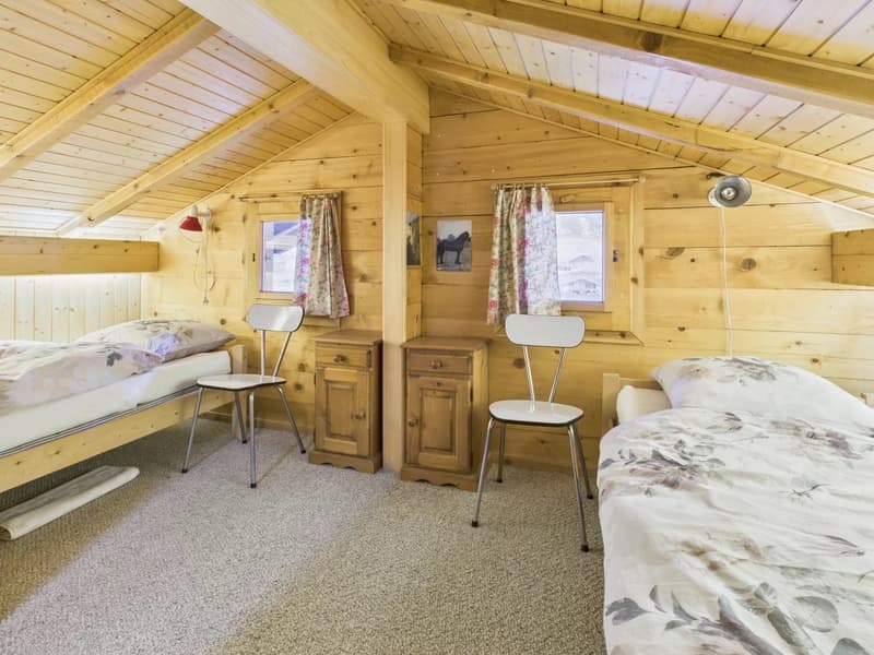 Bedroom with wooden walls, two single beds, two chairs, two nightstands, and two windows with curtains