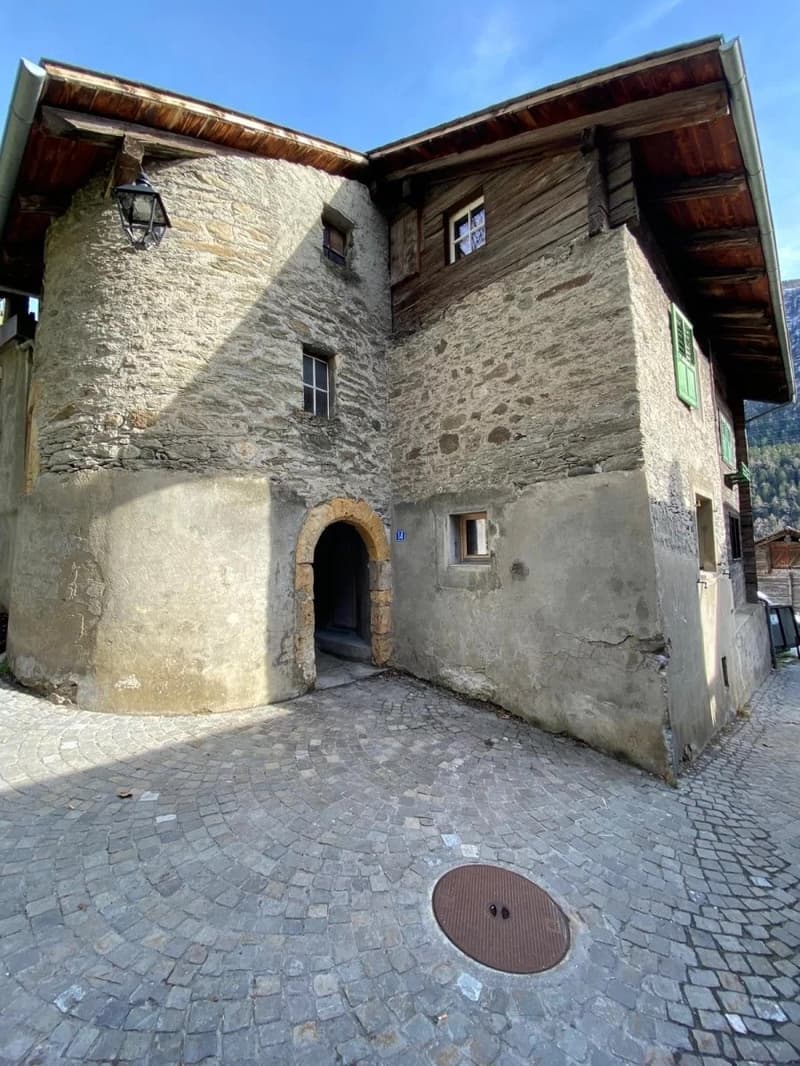 Stone building, wooden roof, arched entrance, green shutters, cobblestone street