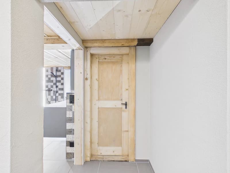wooden door, white walls, wooden ceiling, tiled floor, bathroom visible through the door