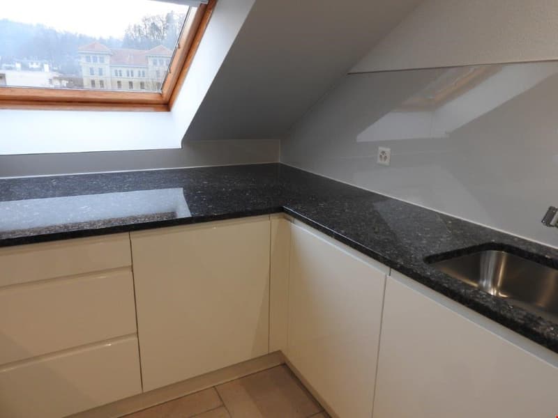 modern kitchen with granite countertops, white cabinets, stainless steel sink, skylight window