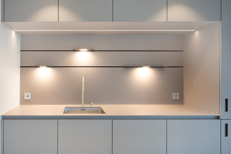 Modern kitchen with grey cabinets, built-in lighting, stainless steel sink, and a dishwasher