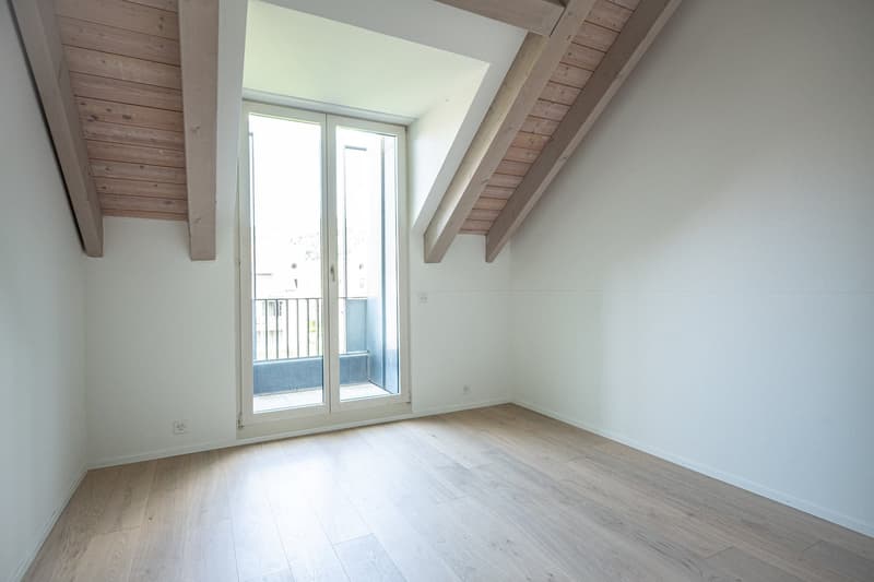 Spacious bedroom with wooden ceiling beams, large windows, and access to a balcony or terrace.
