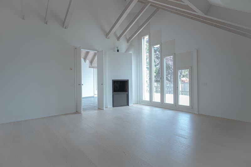 Spacious living room with high ceilings, exposed wooden beams, large windows, and a fireplace