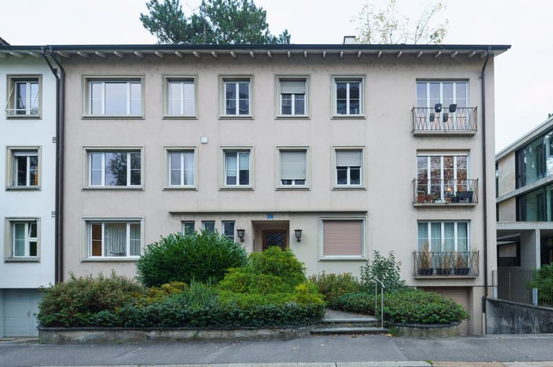4 story building, beige exterior, multiple windows, balconies, entrance with door and lamps, garden in front