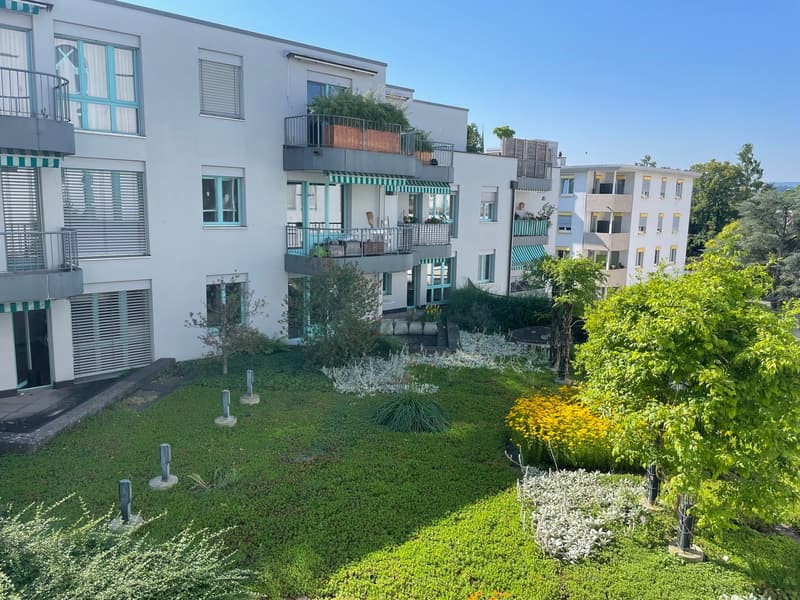 white apartment buildings with multiple balconies, green garden in the middle, lush trees