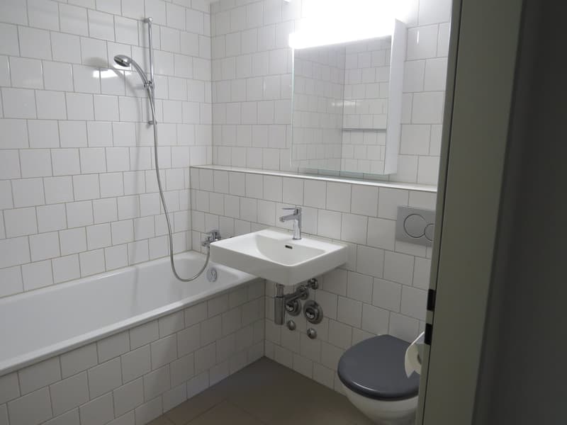 white tiled walls and floor, bathtub, shower head, vanity sink, toilet, mirror