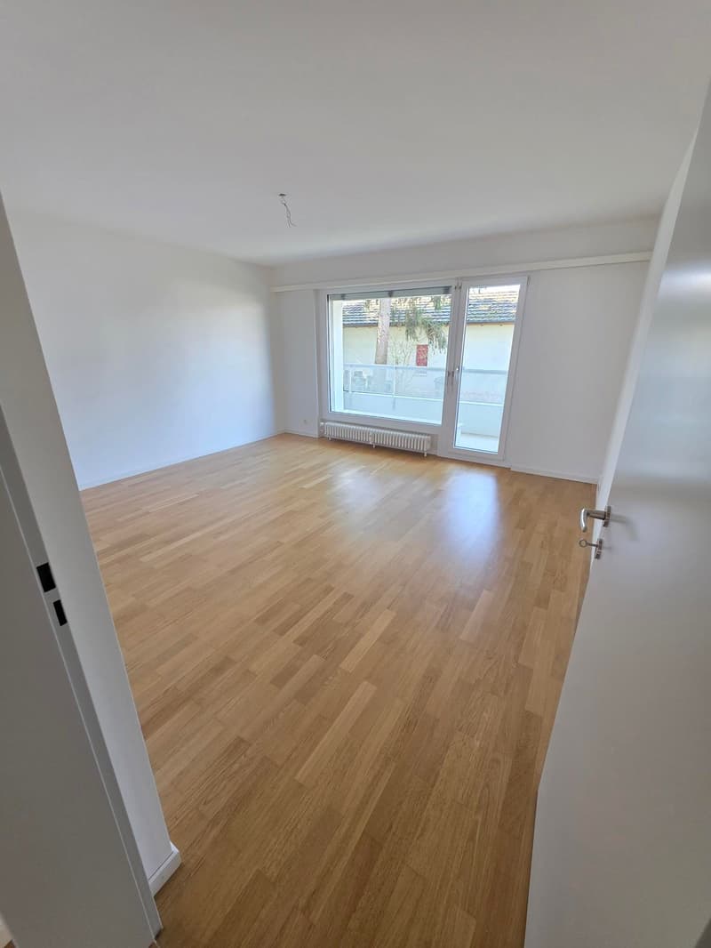 empty room with wooden floor, sliding glass door leading to balcony, white walls