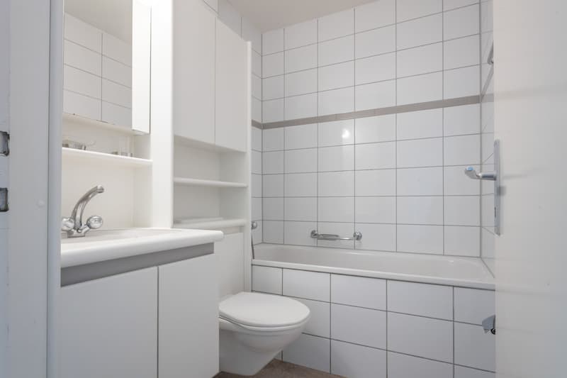 white tiles, white bathtub, white toilet, white sink, white cabinets, silver faucet