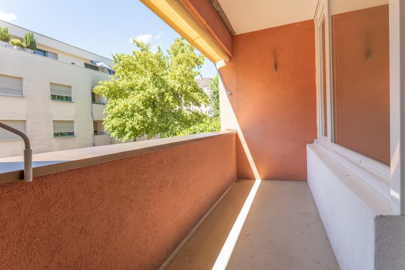 Balcony with a view of a tree and a building, orange walls, white floor, glass window