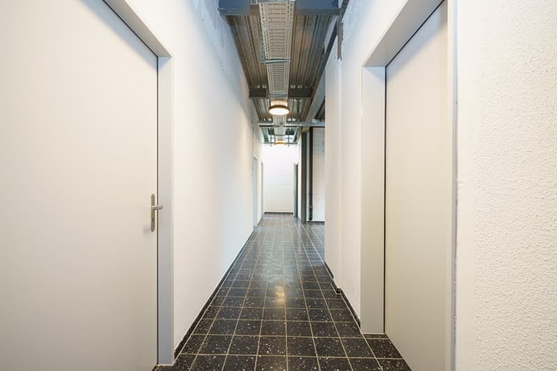 Empty hallway with white walls, black tiled floor, white doors, and ceiling lights.