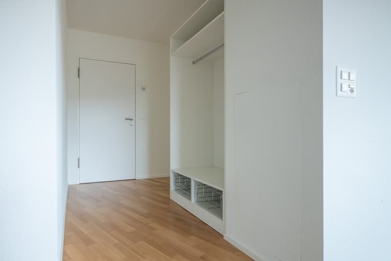 Empty room with white walls, wooden floor, white door, built-in wardrobe, and power outlet.