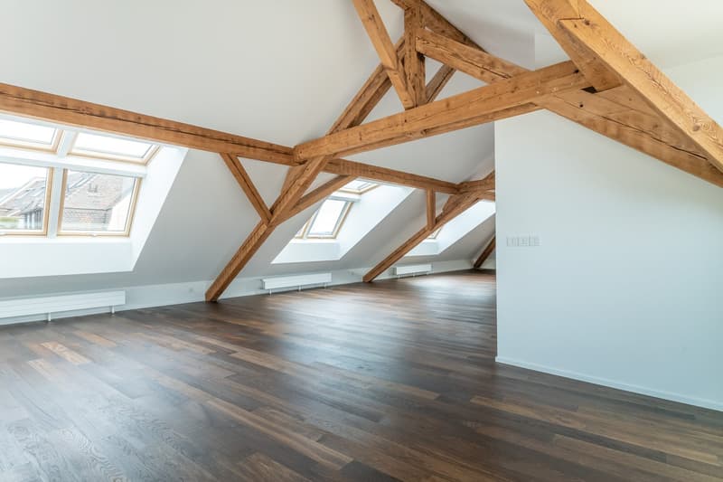 Large open attic space with exposed wooden beams, hardwood flooring, and skylights providing natural light. The space appears to be a potential living or studio area with ample room and a cozy, rustic feel.