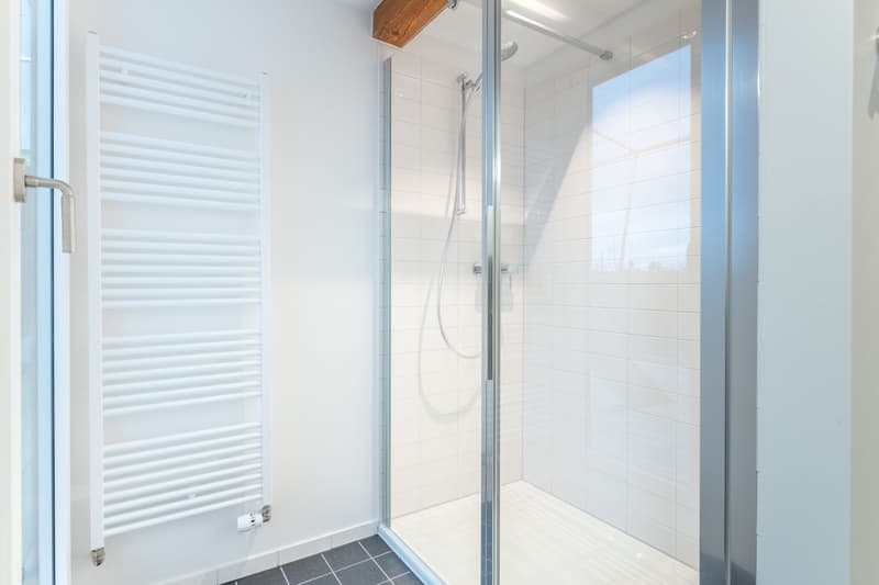 Spacious bathroom with white tiled walls, glass shower enclosure, and a towel warmer radiator.