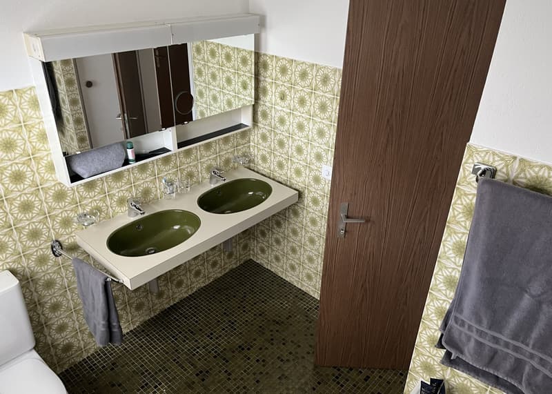 Bathroom with double sink, mirror, towel rack, toilet, tiled floor, wooden door