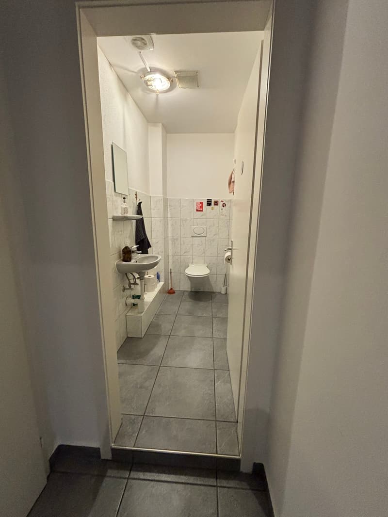 Tiled floor, white walls, sink, toilet, mirror, lighting fixture