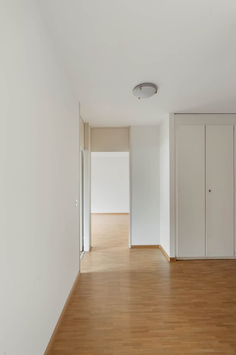 Empty room with white walls, wooden floor, ceiling light, open door, double doors on the right side