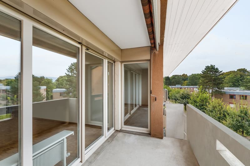 spacious balcony, large sliding glass doors, wooden flooring, concrete floor, trees and buildings in background