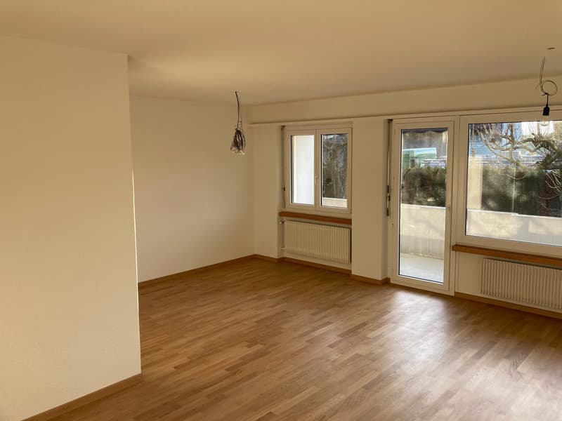 Empty room with wooden floor, white walls, radiators, sliding doors to a balcony