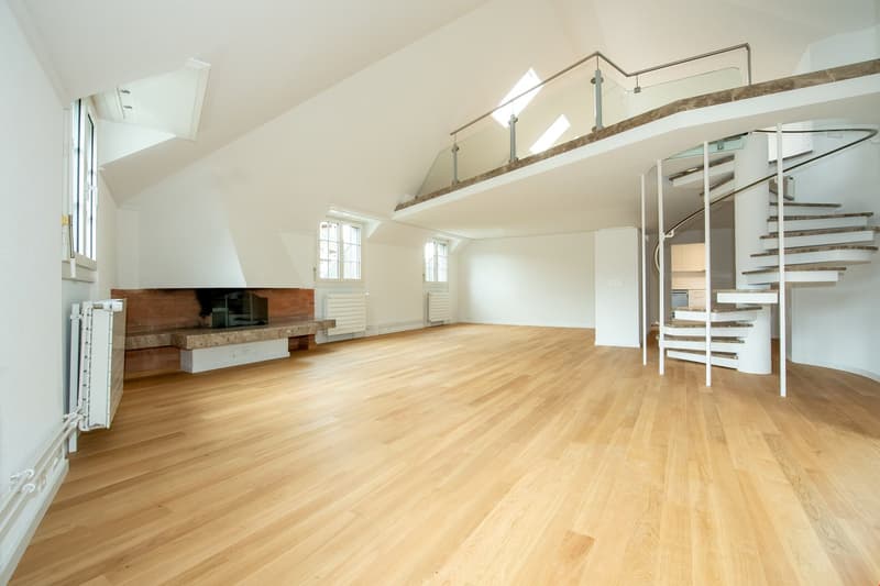 Empty room with wooden floor, white walls, fireplace, spiral staircase, windows, radiators
