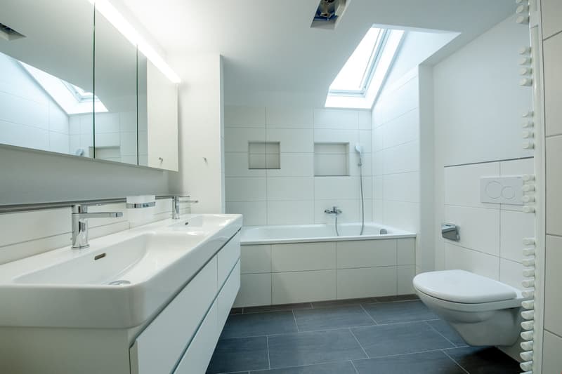 modern bathroom with white tiles, bathtub, double sink, toilet, skylights