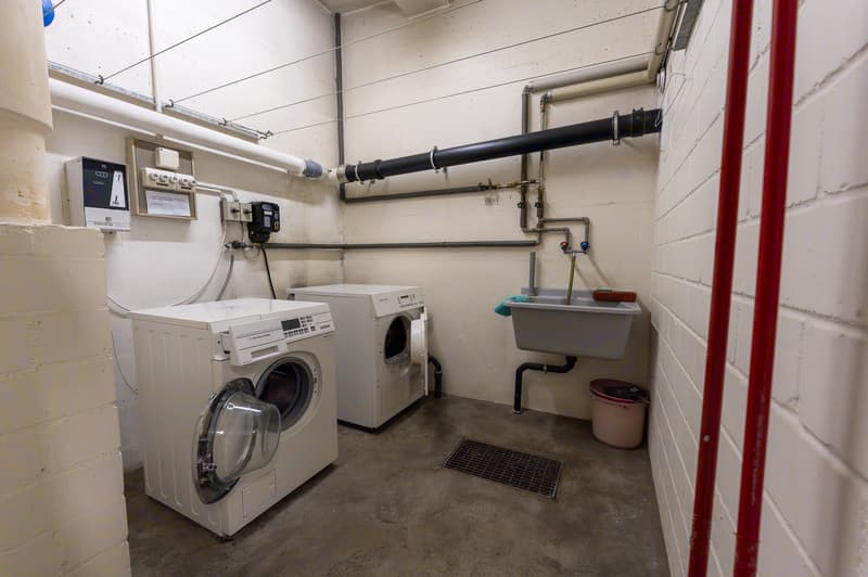 A utility room with white walls, two washing machines, and a sink.