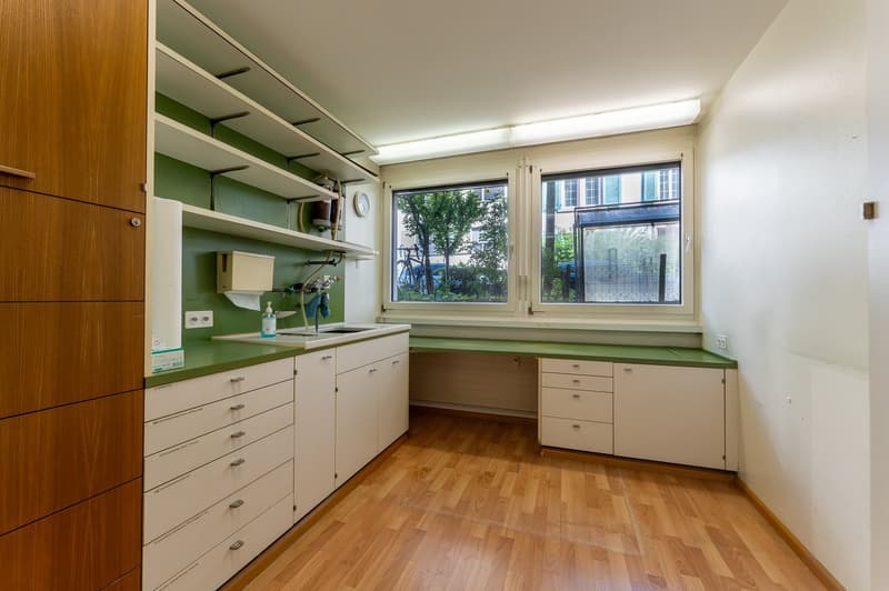 washroom with wooden and green shelves, white drawers, sink, and toilet paper holder