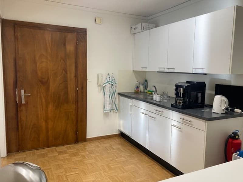 Modern equipped kitchen with wooden door, white cabinets, black countertop, gas stove, coffee maker, toaster, refrigerator, electric kettle