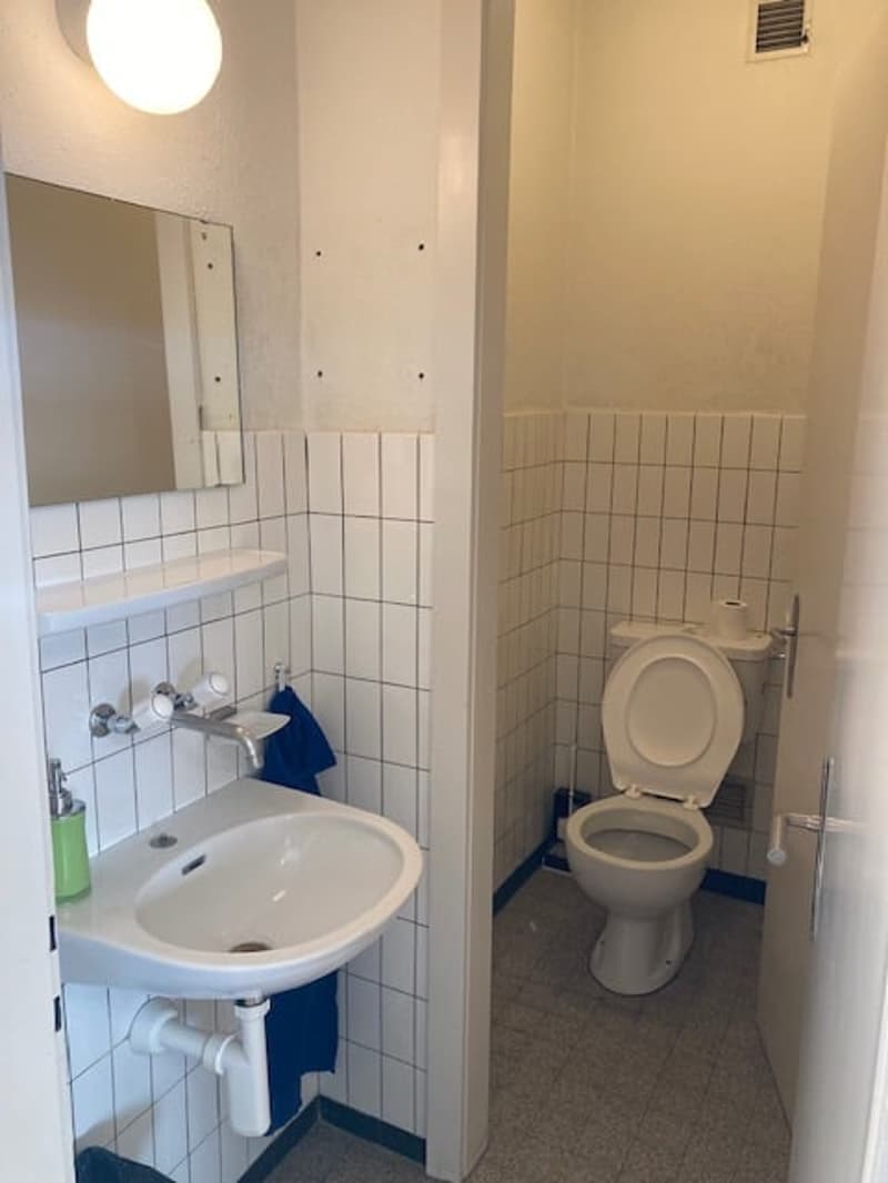 bathroom with white tiles, white sink, white toilet, toilet paper holder, mirror, and a blue towel
